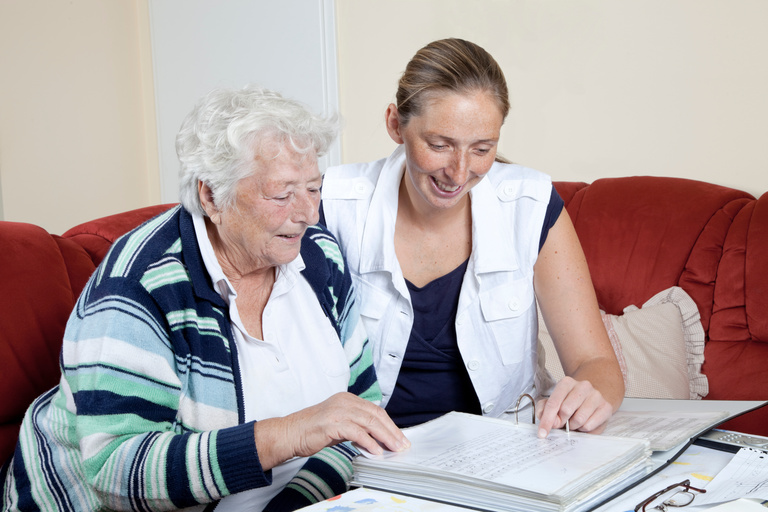 Ältere Person liest mit Hilfe von Pflegerin Unterlagen